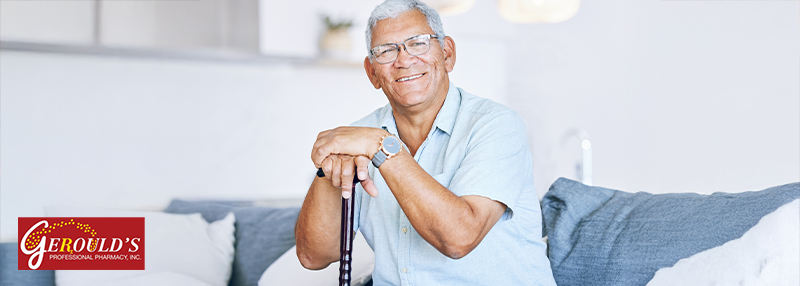 Senior man smiling while sitting on a couch with his hands on top of a cane handle