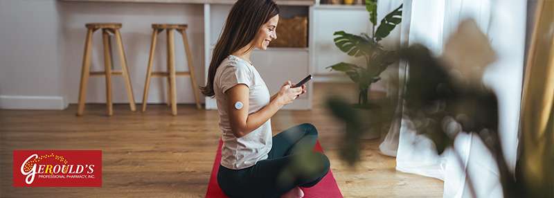 Woman sitting on yoga mat on her phone with continuous glucose monitor on her arm