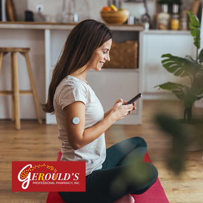 Woman sitting on yoga mat on her phone with continuous glucose monitor on her arm
