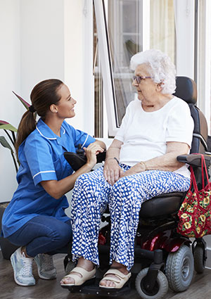 home nurse kneeling next to elderly woman